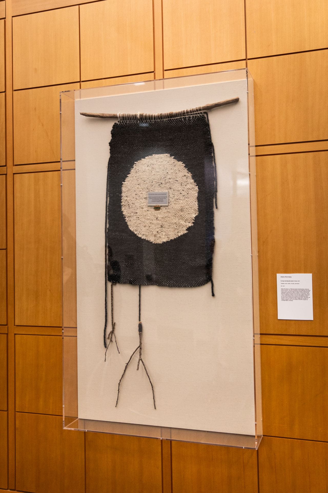 Tapestry hanging from large stick. Tapestry is black with white circle in the middle, and a circuit board in the middle of the circle. 