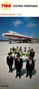 Header "TWA System Timetable effective February 1, 1970." Under header is a photo of an in-flight crew including pilots and flight attendants standing on a runway with a TWA 747 in the background. 