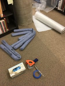 roll of plastic, blue water socks, and tape on brown carpet
