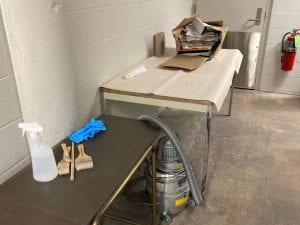 2 tables with a cardboard box, vacuum, gloves, and brushes on them