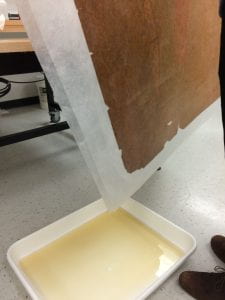 Piece of brown paper on a white sheer cloth held over a white tray with brown water in it.