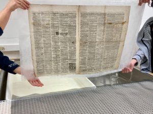 4 hands holding a newspaper page up