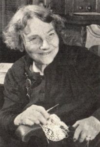 black & white photograph of Janie Brady Jones holding a piece of needlework in progress and smiling