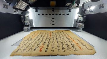 Black and red arabic script on brown paper in a lighted grey chamber.