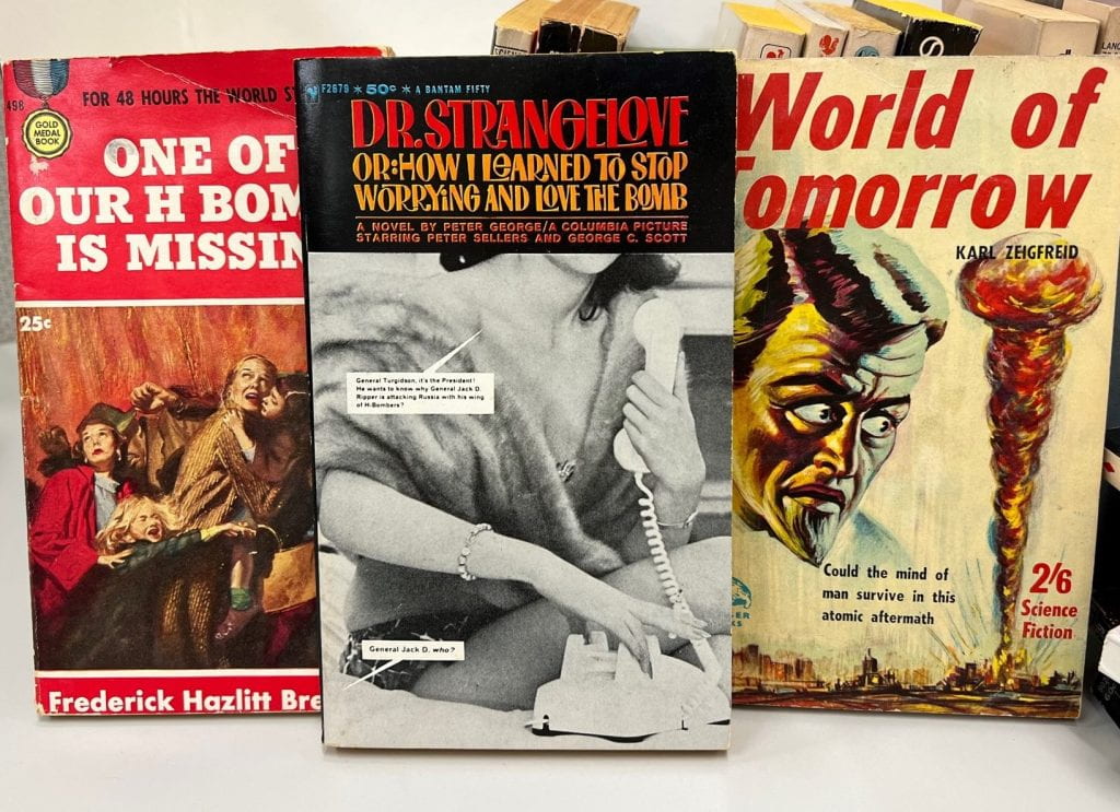 Paperback books in a row showing the illustrative covers dealing with atomic bombs.