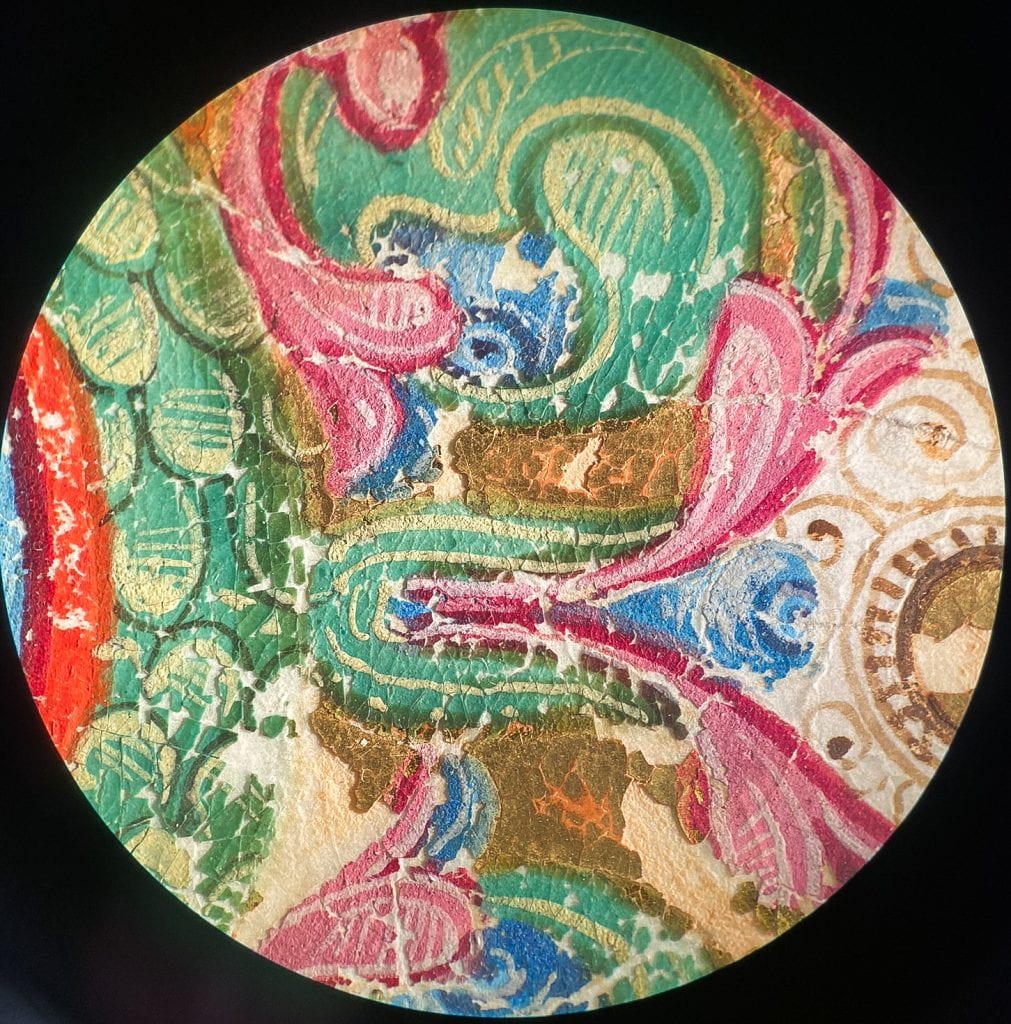 Detail through the microscope at a section of the front page, showing the condition of the pink and green pigments and the gilded areas.