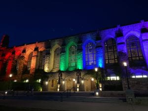 A nighttime image of the exterior of Deering Library, a large gothic building. The stone walls are lit in rainbow coloration.