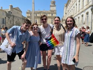 five people standing together, holding a rainbow gay pride flag