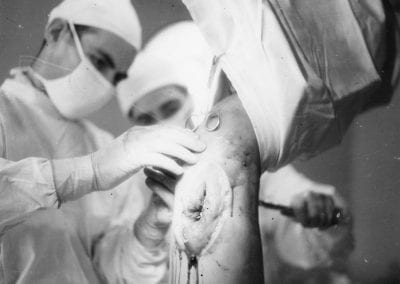 Two doctors performing surgery on a bloody leg wound