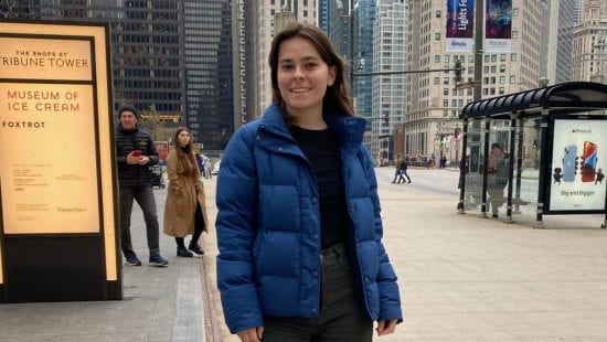 Kate stands smiling in downtown Chicago wearing black jeans and a blue puffy jacket