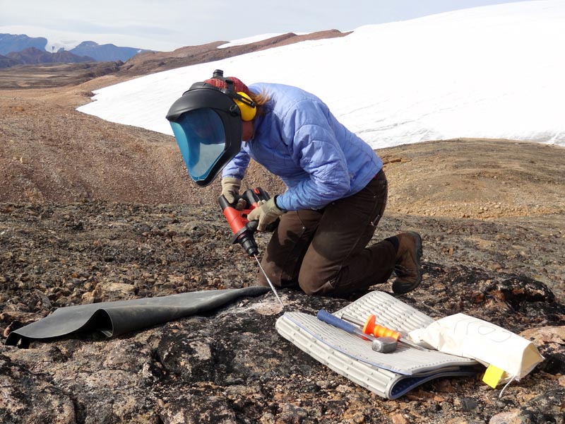 Laura sampling a bedrock surface for cosmogenic surface exposure dating. Renland Ice Cap in background.